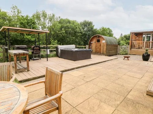 Patio at cottage with hot tub, outdoor seating, barbecue and wooden sauna hut