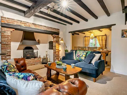 Cottage lounge with exposed beams, brick fireplace, sofas and view into dining area