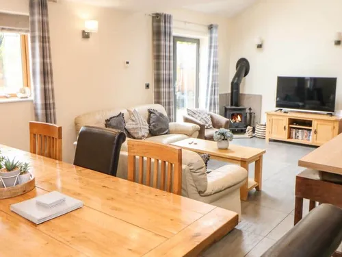 Cottage living room with wood burner, sofa, TV and dining table in foreground