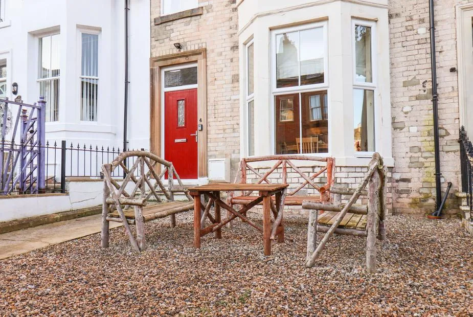4 Normanby Terrace brick frontage with red door, bay window, and rustic wooden seating on gravelled garden