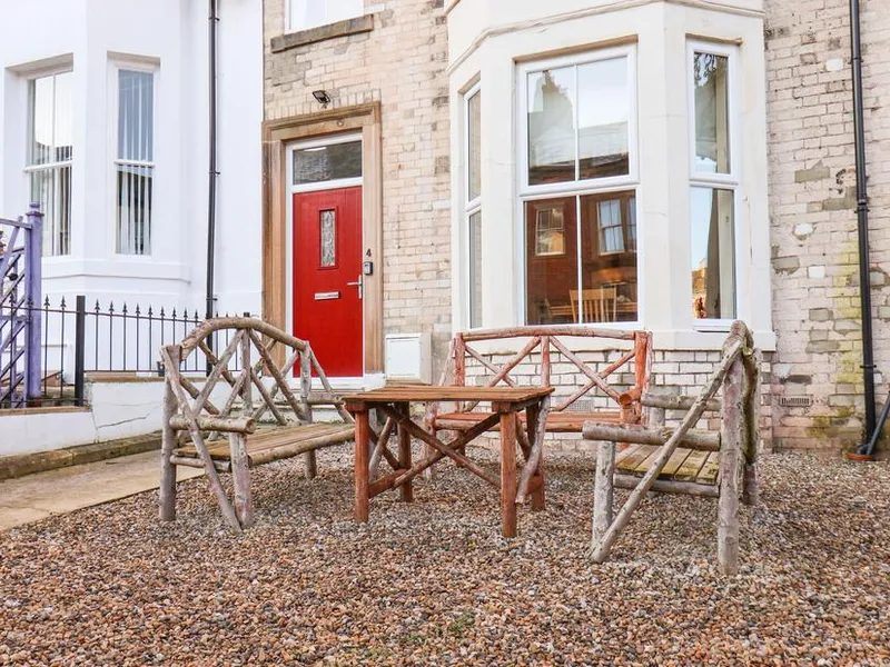 4 Normanby Terrace brick frontage with red door, bay window, and rustic wooden seating on gravelled garden