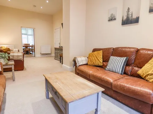 Sitting room with tan leather sofas, mustard cushions, and grey coffee table with dining area beyond