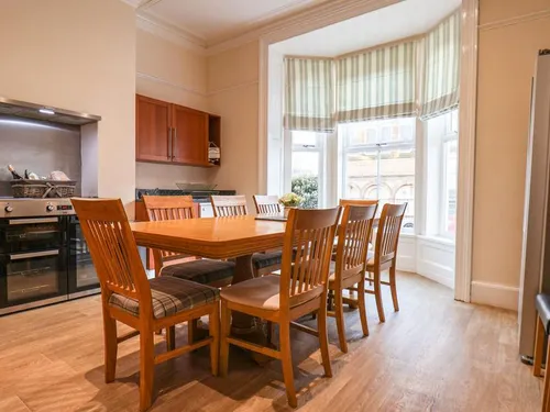 Kitchen-diner with wooden table, tartan-cushioned chairs, and large bay window with striped blind