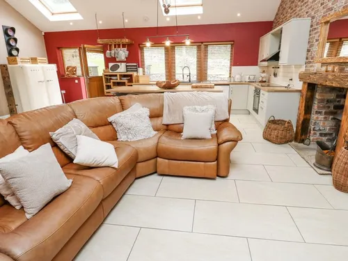Open-plan living space with tan leather corner sofa, exposed brick fireplace with woodburning stove, and skylights above