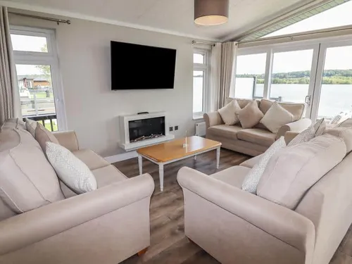 Living room with sofas, wall-mounted TV, fireplace and lake view through windows