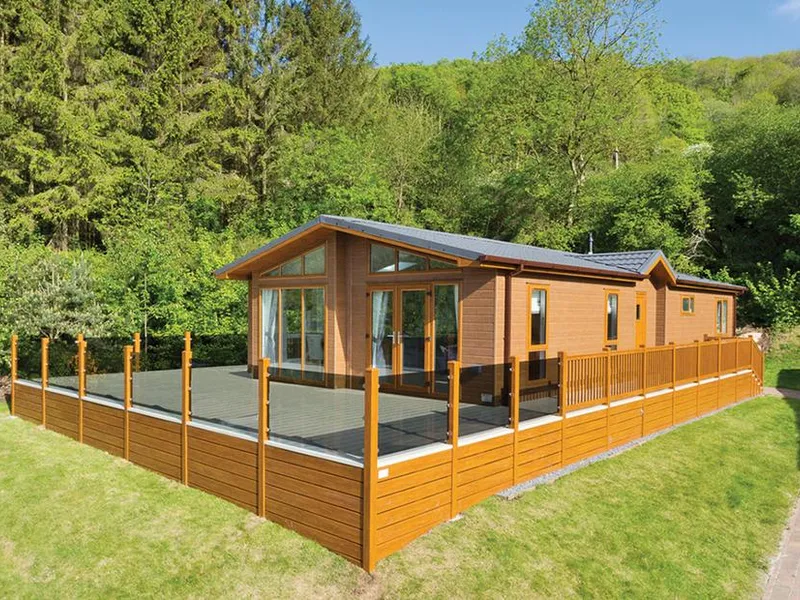 Ashton Elegance Premier lodge with glass-panelled decking and wooded Mendip hillside behind