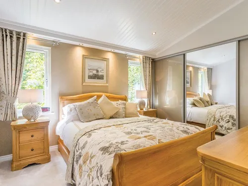 Double bedroom with oak sleigh bed, floral throw, and mirrored sliding wardrobes