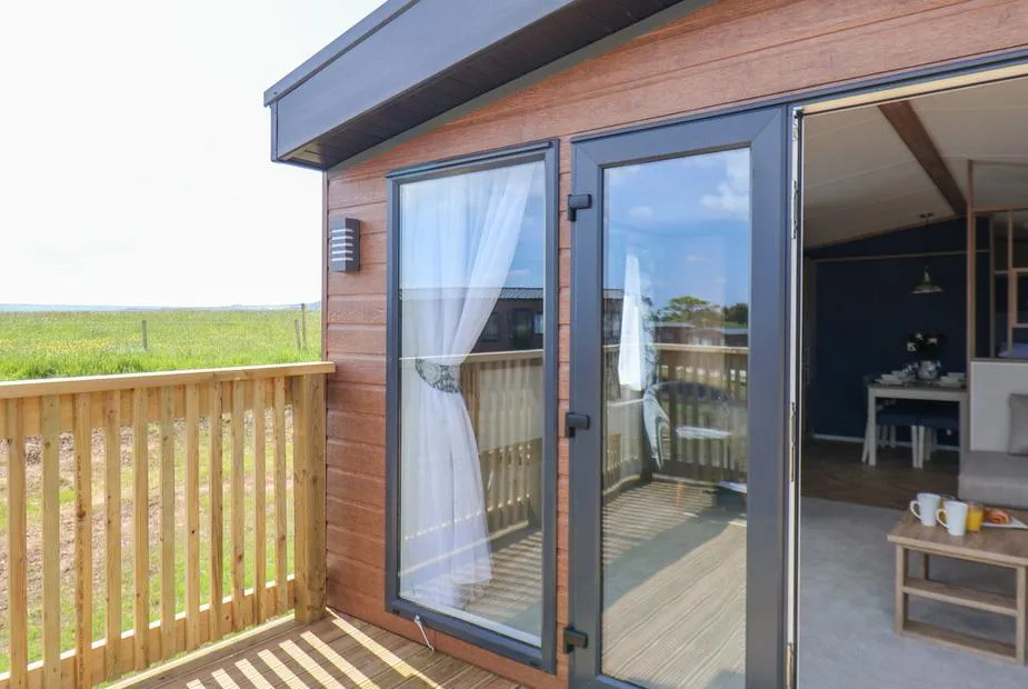Timber-clad lodge with glass double doors, decking, and open countryside views