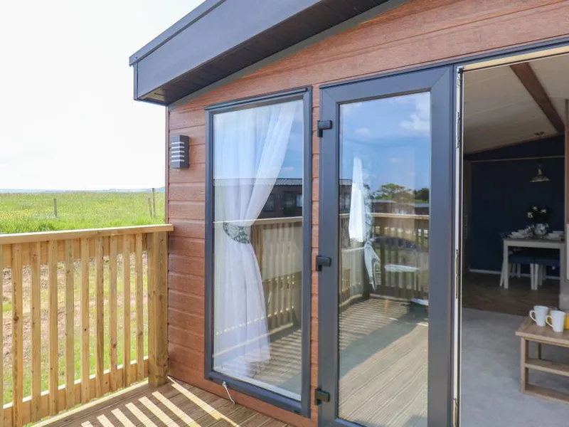 Timber-clad lodge with glass double doors, decking, and open countryside views