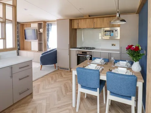 Open-plan kitchen and dining area with herringbone flooring, blue chairs, and wall-mounted TV