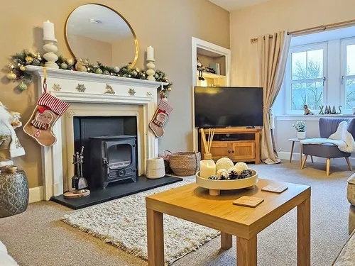 Cosy living room with wood burner, Christmas stockings on the mantelpiece, and TV beside a window