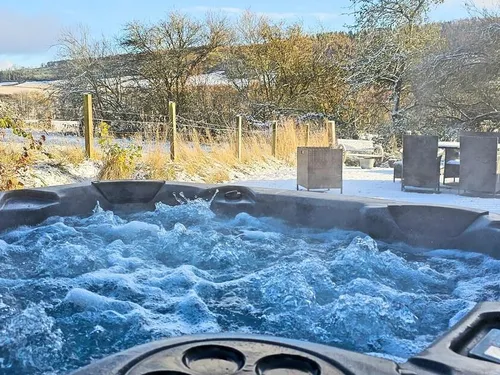 Hot tub steaming in a snow-covered garden with Highland countryside views