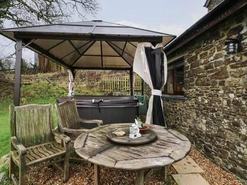 Cottage patio with wooden chairs, round table and covered hot tub