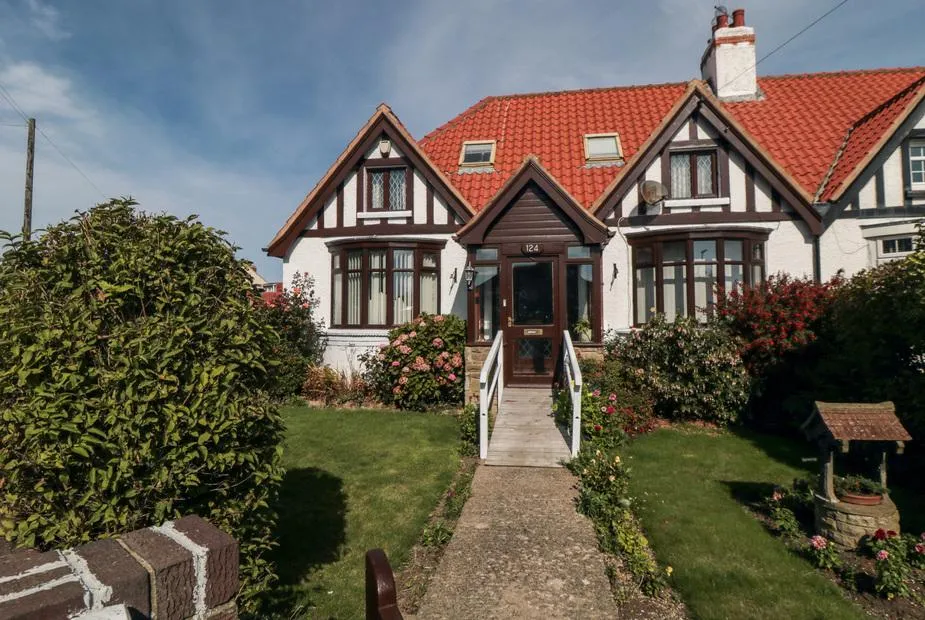 Beachcrest cottage with Tudor-style half-timbered gables, red tile roof, and front garden with flowering shrubs
