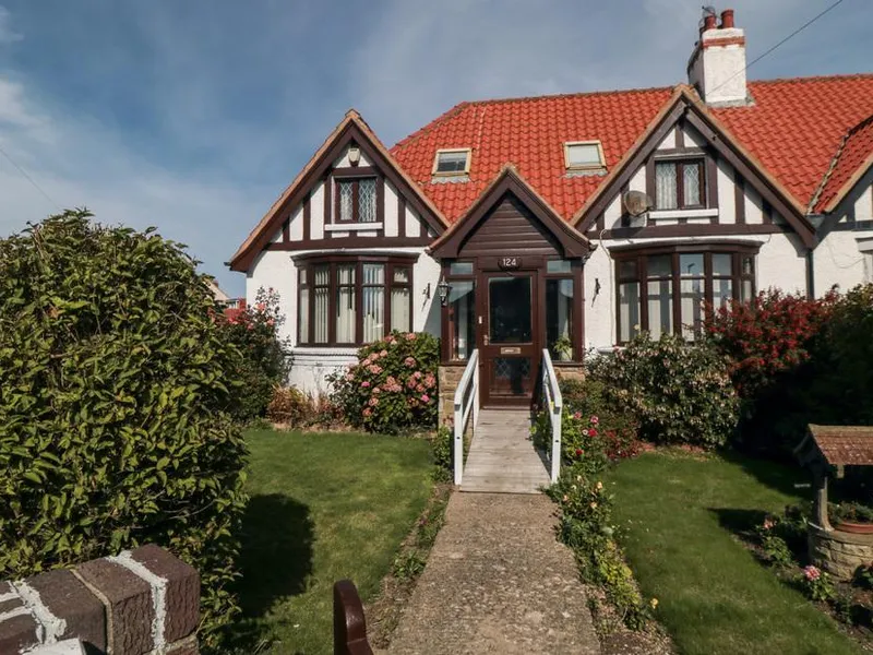 Beachcrest cottage with Tudor-style half-timbered gables, red tile roof, and front garden with flowering shrubs
