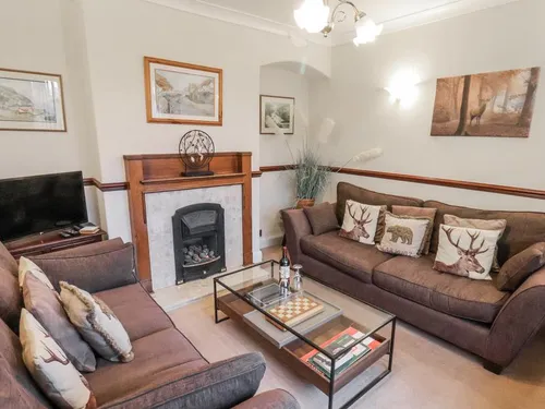 Sitting room with brown sofas, stag-print cushions, marble fireplace with gas fire, and glass coffee table