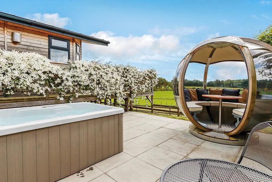Hot tub and rotating garden pod on a paved patio with flowering clematis and open meadowland views