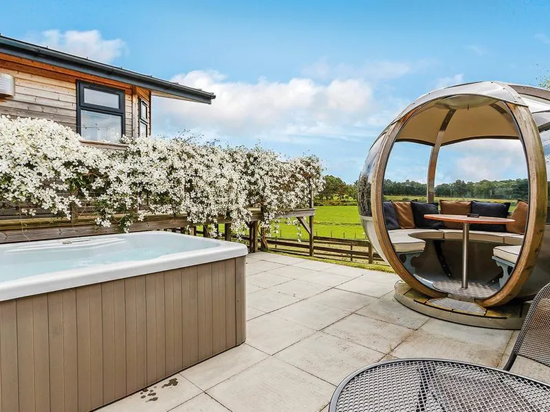 Hot tub and rotating garden pod on a paved patio with flowering clematis and open meadowland views