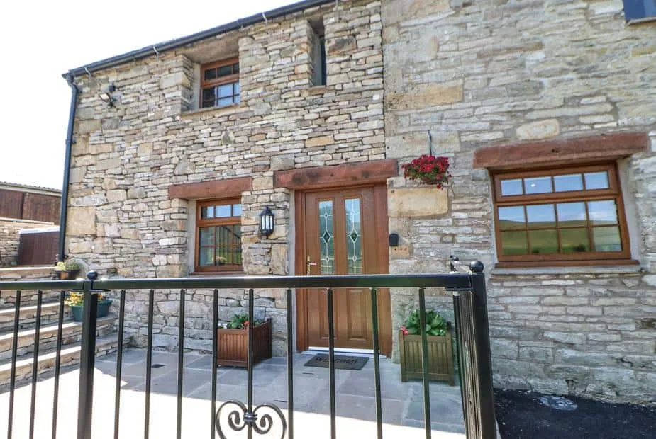 Stone exterior of Birkett Barn with wooden door, iron gate, and flower planters visible.