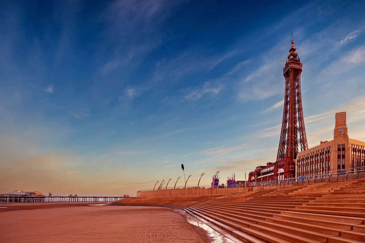 Sunrise over Blackpool promenade featuring the iconic Tower and empty steps leading to the beach, capturing a peaceful morning atmosphere.