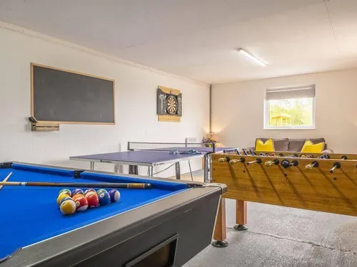 Cottage games room with pool table, table tennis, foosball, dartboard, and sofa.