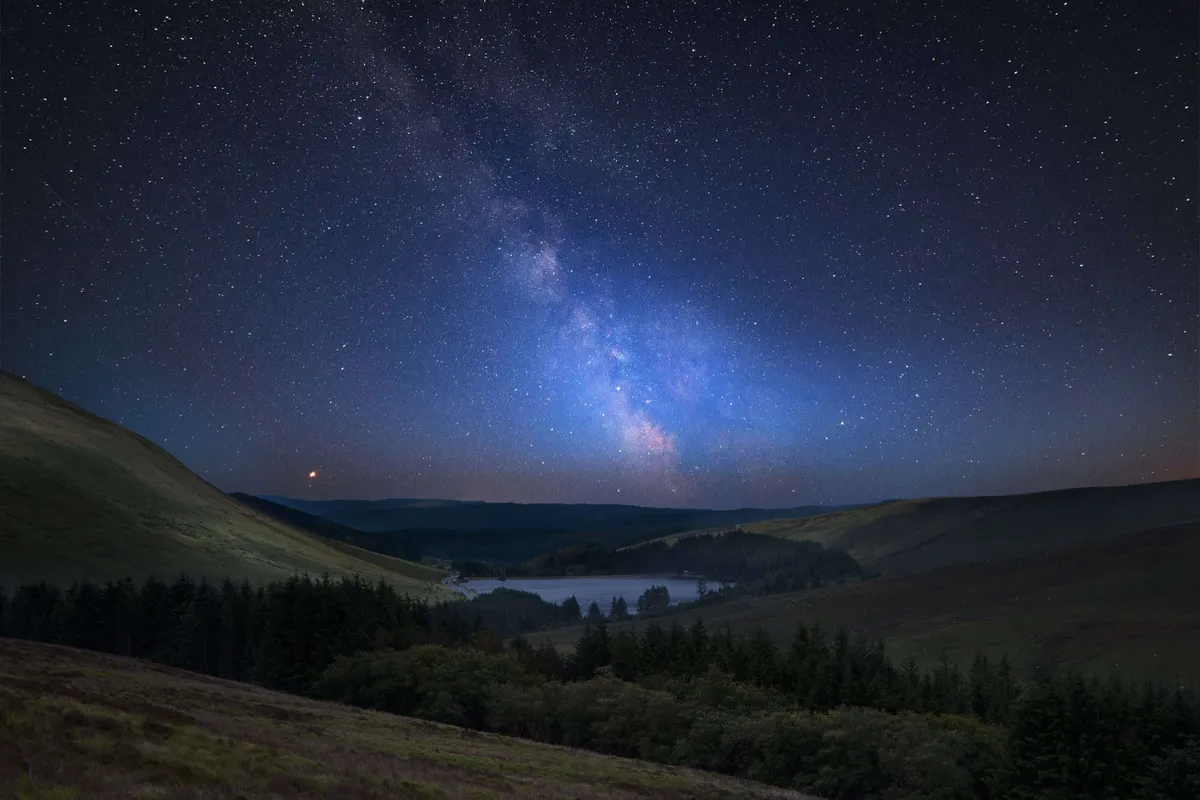 The Milky Way shining over a serene mountain lake in the Brecon Beacons Dark Sky Reserve.