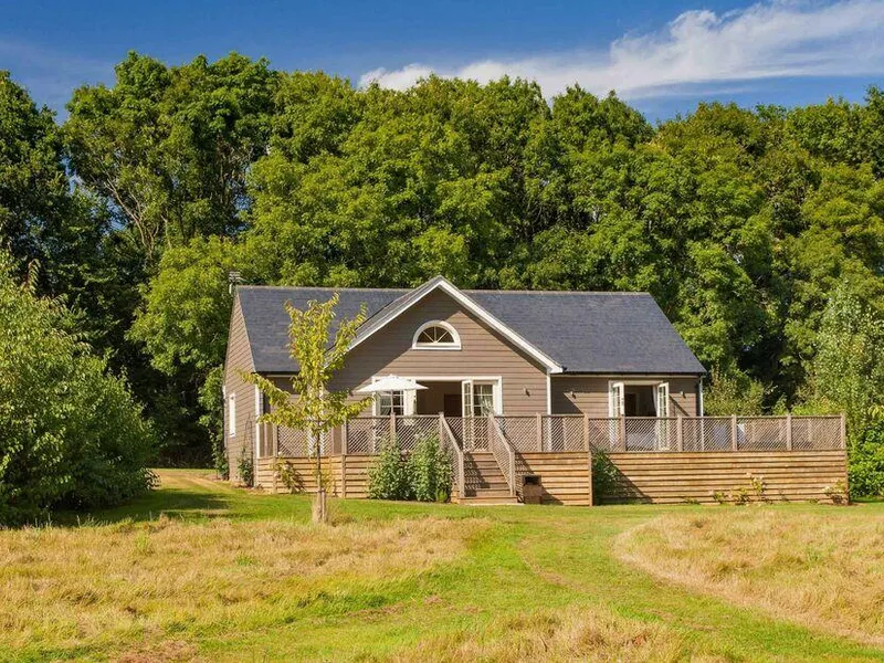 Brook Lodge with large wooden deck, set in grassy clearing by woodland