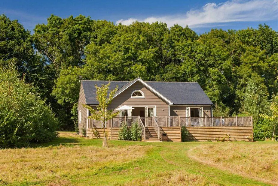 Brook Lodge with large wooden deck, set in grassy clearing by woodland