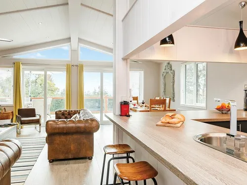 Open-plan kitchen with breakfast bar, leather Chesterfield sofas, and vaulted ceiling with patio doors