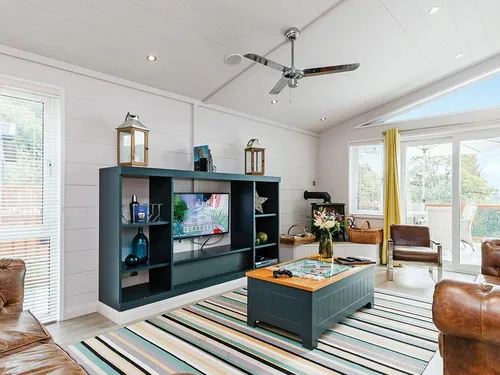 Lodge lounge with flatscreen TV, leather Chesterfield sofas, striped rug, and patio doors to decking