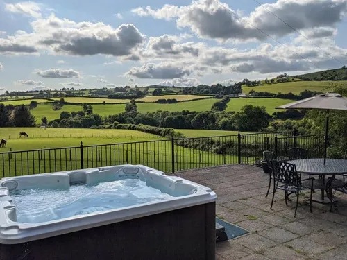 Cottage patio with hot tub and outdoor table overlooking rural fields and hills