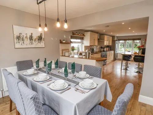 Open-plan dining area with table set for eight and pendant lights, leading into kitchen with cream units and oak worktops