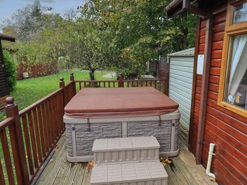 Lodge decking with covered hot tub and steps next to wooden exterior wall