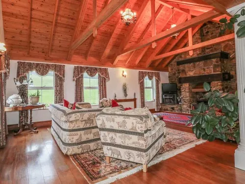 Cottage lounge with exposed wooden beams, stone fireplace, and patterned sofas