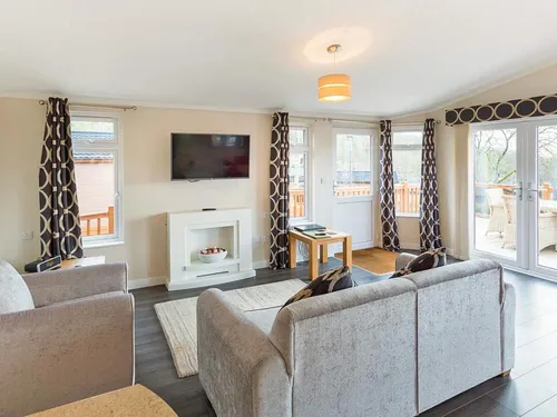 Living room with grey sofas, white electric fireplace, wall-mounted TV, and patio doors to the deck
