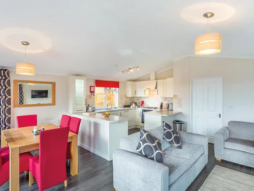 Open-plan kitchen and dining area with red chairs, oak table, cream units, and grey sofa