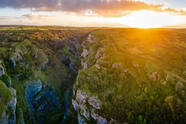 Aerial view of Cheddar Gorge at sunset, with golden light illuminating the dramatic limestone cliffs and the rolling Mendip Hills.