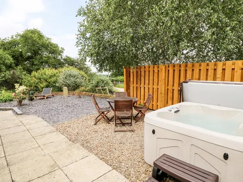 Cottage garden with hot tub, wooden table and chairs, gravel and patio area