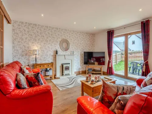 Cottage lounge with red sofas, fireplace and sliding doors to garden patio with chairs