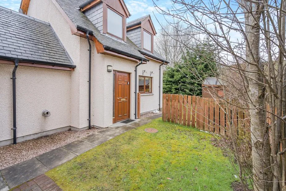Coire Cas cottage exterior with wooden door and small fenced garden area