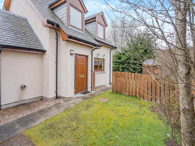 Coire Cas cottage exterior with wooden door and small fenced garden area