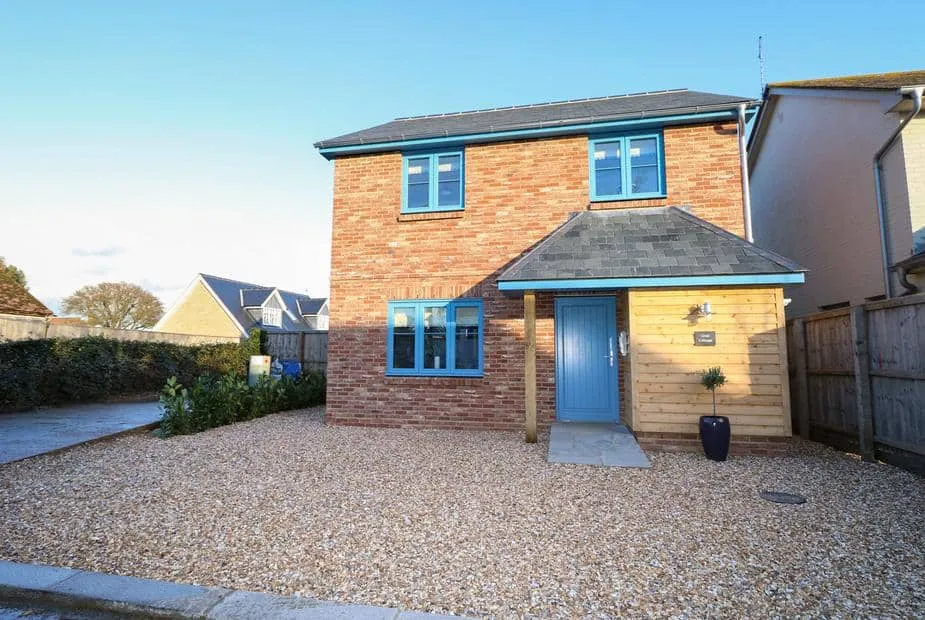 Crab Cottage exterior with red brick walls, blue windows, and gravel driveway