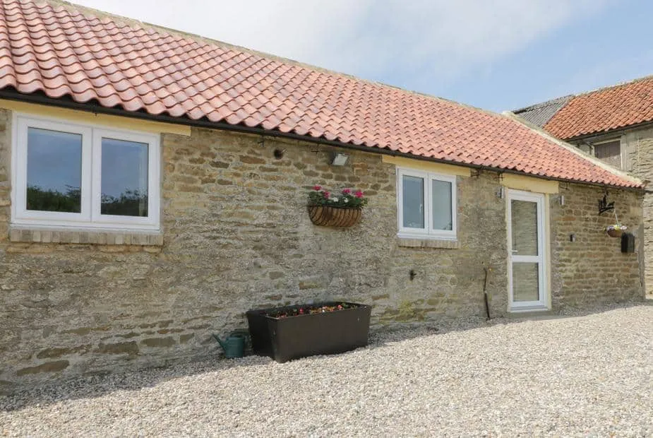 Stone exterior of Crabtree Cottage with red tiled roof and flower planters by the entrance.