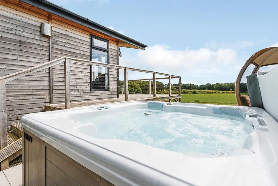 Bubbling hot tub beside the lodge decking with open meadowland views and garden pod