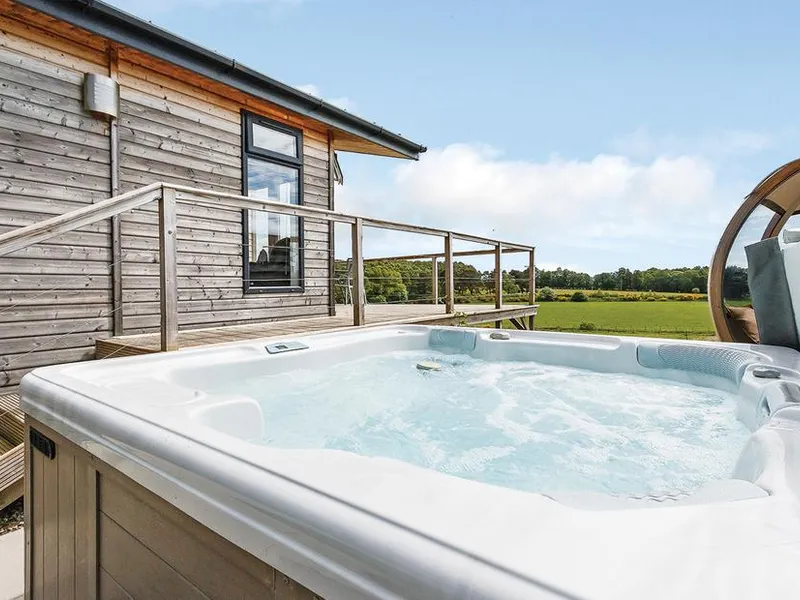 Bubbling hot tub beside the lodge decking with open meadowland views and garden pod