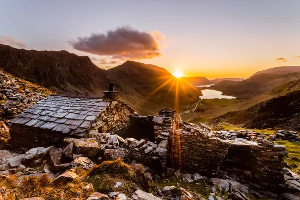Sunset over the wild Cumbrian landscape with a historic stone bothy and rolling green valleys.