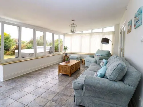 Cottage sunroom with large windows, tiled floor and two sofas around a wooden coffee table