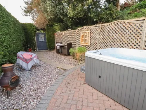 Cottage garden with hot tub, patio table and chairs, chiminea, and trellis fencing