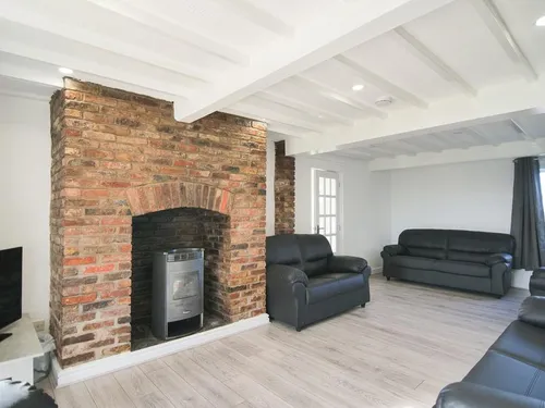 Living room with exposed brick fireplace, electric woodburner, black leather sofas, and beamed ceiling