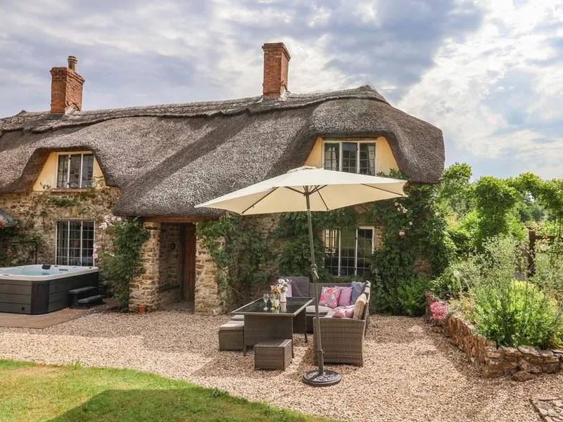 Traditional stone holiday cottage featuring a hot tub and patio with an umbrella